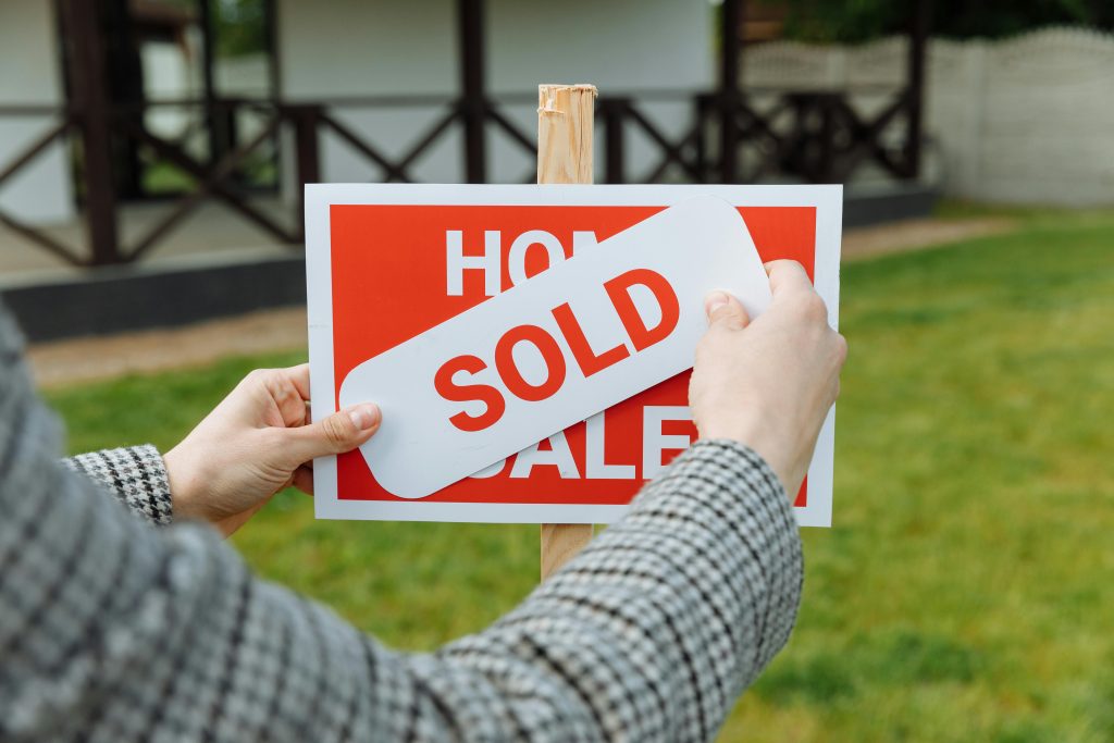 "SOLD" sign over a "HOME FOR SALE" sign in front of a house, symbolizing a successful home sale in Las Vegas.